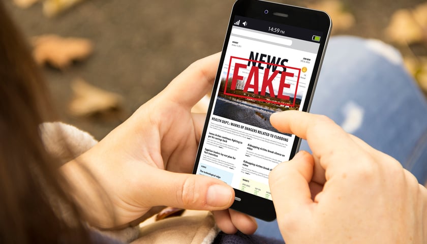Zbliżenie na smartfon, na którego ekranie wyświetla się napis "Fake news"