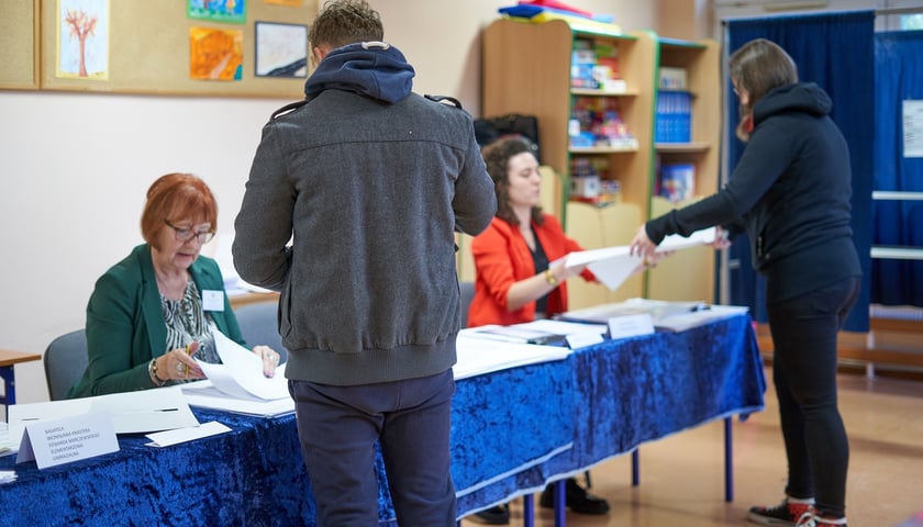 Siedziba Obwodowej Komisji Wyborczej we Wrocławiu. Na zdjęciu dwie osoby odbierają karty wyborcze od członków komisji. Zdjęcie ilustracyjne
