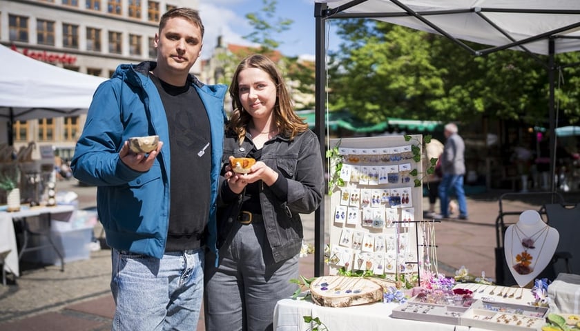 Kobieta i mężczyzna stoją obok siebie na placu Solnym i pokazują produkty kupione na bazarze rękodzieła