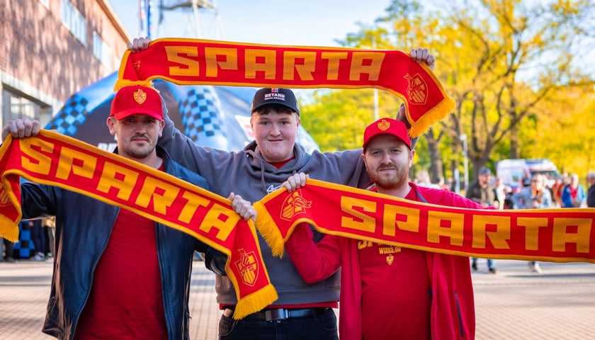 Trzech kibiców Sparty Wrocław z uniesionymi klubowymi szalikami przed meczem na Stadionie Olimpijskim 