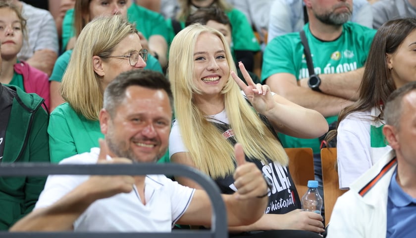 Uśmiechnięta kobieta i inny kibice na trybunie Hali Stulecia na meczu Śląska z Górnikiem