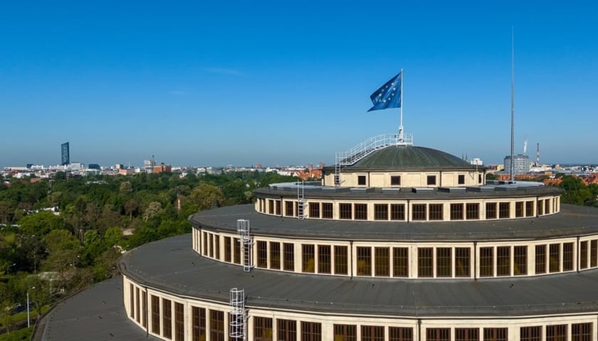 Kopuła Hali Stulecia z flagą unijną. Na zdjęciu na dachu dużej budowli powiewa niebieska flaga