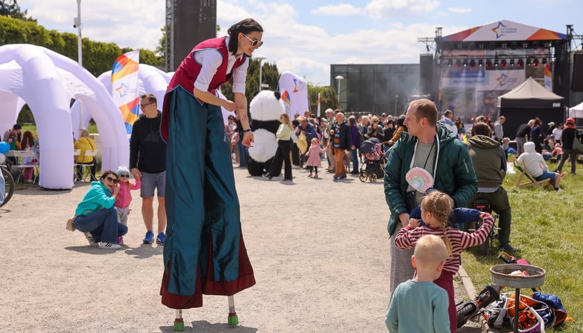 Piknik na Pergoli z okazji Dni Funduszy Europejskich. Na zdjęciu dziewczyna na szczudłach bawi się z dzieckiem i mężczyzną