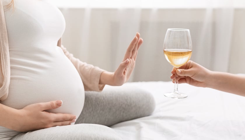 Kobieta w ciąży odmawiająca wypicia kieliszka wina, siedząca w komfortowym wnętrzu.