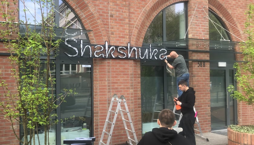 Na zdjęciu pracownicy zawieszający logo restauracji Shakshuka przy ul. Braniborskiej we Wrocławiu.