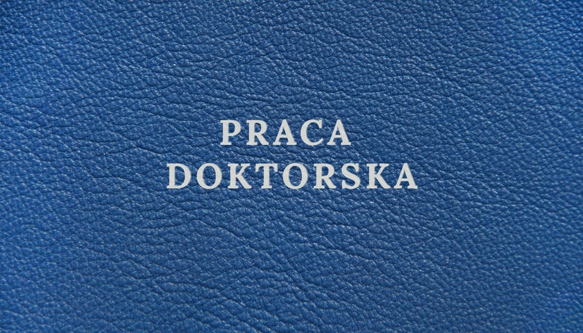 Zdjęcie okładki. Granatowa okładka ze srebrnym napisem "PRACA DOKTORSKA"