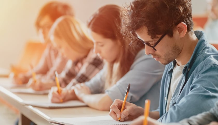 Studenci siedzą na wykładzie i notują.