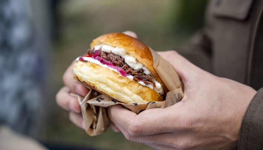Na zdjęciu osoba trzymająca w dłoniach burgera podczas wrocławskiej imprezy Gastro Miasto na bulwarze X. Dunikowskiego.
