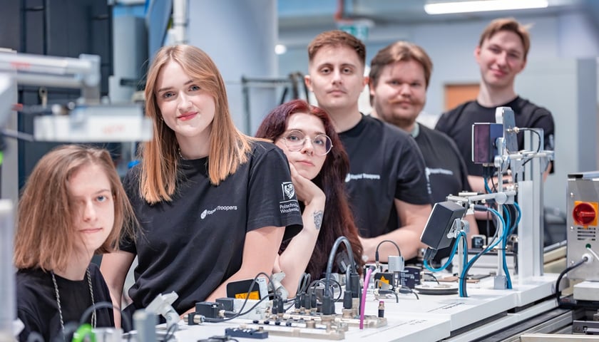 Studenci z Koła Naukowego Rapid Troopers z Politechniki Wrocławskiej. Na zdjęciu młode kobiety i mężczyźni przy stole z urządzeniami technicznymi