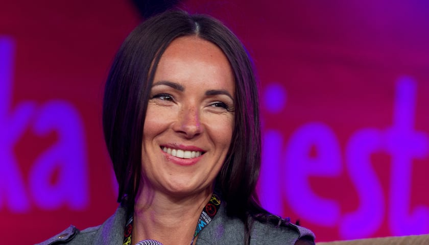 Kasia Kowalska. Na zdjęciu uśmiechnięta młoda kobieta w długich włosach
