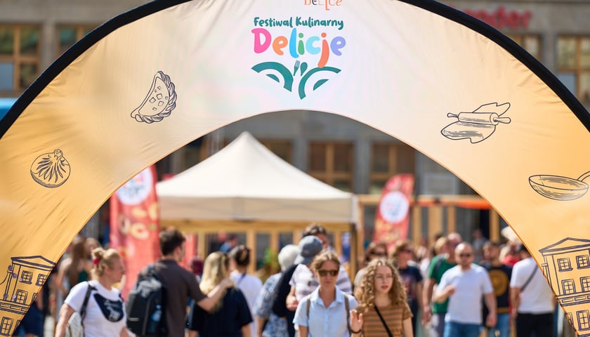 Tłum ludzi pod łukiem dekoracyjnym z napisem Delicje