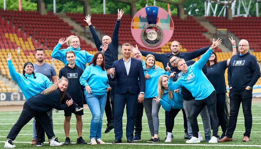 Grupa osób z MCS Wrocław na płycie stadionu Olimpijskiego, w kółku jest medal 11. PKO Nocnego Wrocław Półmaratonu 