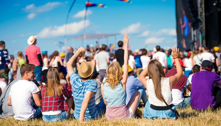 Na zdjęciu koncert w plenerze, widać rozbawionych ludzi siedzących na trawie