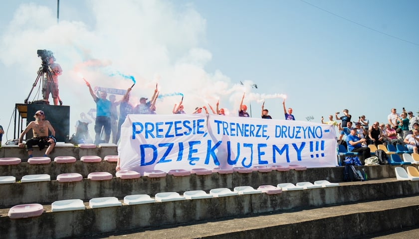 Kibice Polaru na trybunach z transparentem dziękującym za awans. W rękach odpalone race