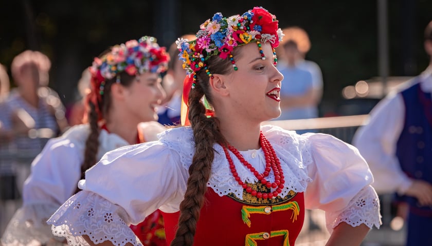 Dwie kobiety w wiankach na głowach i strojach ludowych, w tańcu na pl. Wolności