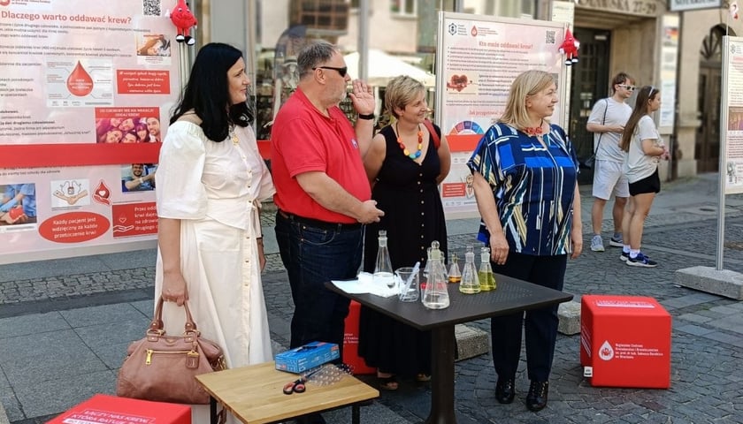 Uroczyste rozpoczęcie Wystawy. Organizatorzy stoją przed stolikami, na których znajdują się akcesoria laboratoryjne.