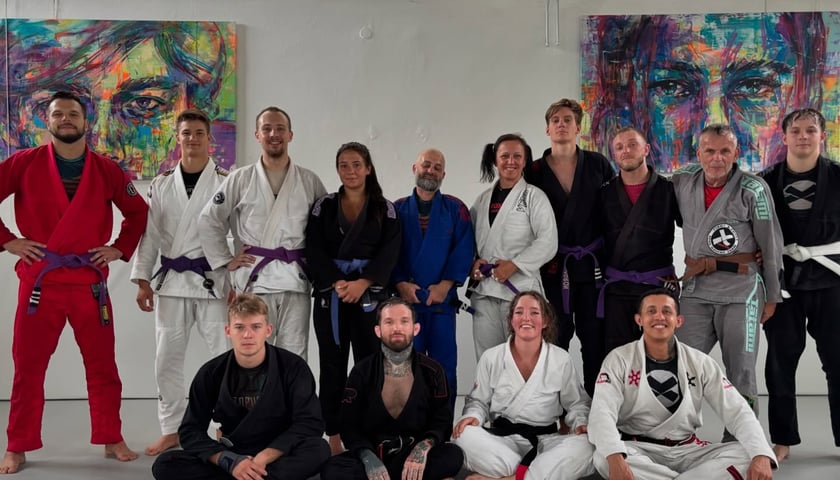 Zawodnicy klubu ju-jitsu WroX Gym Wrocław w kimonach na wspólnym zdjęciu. Dziesięciu zawodników stoi, a czterech siedzi przed nimi.
