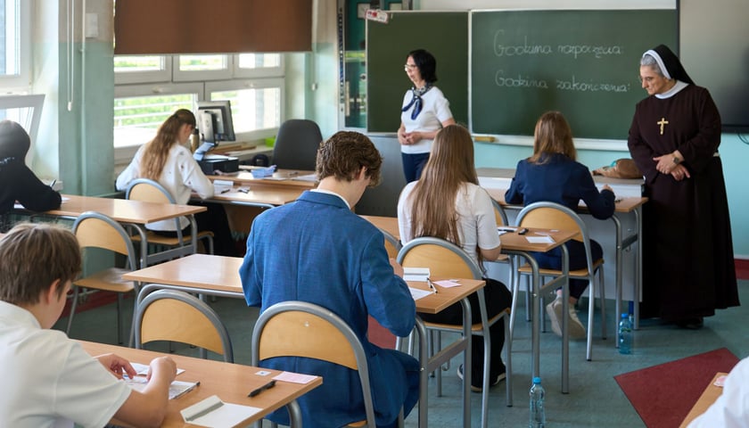 Egzamin ósmoklasisty w maju 2025 we Wrocławiu. Widać uczniów piszących w ławkach testy oraz dwie nauczycielki.