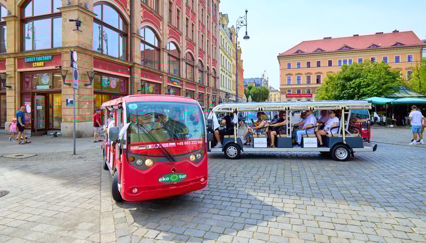 Dwa pojazdy wycieczkowe typu meleks wypełnione ludźmi sfotografowane na pl. Solnym