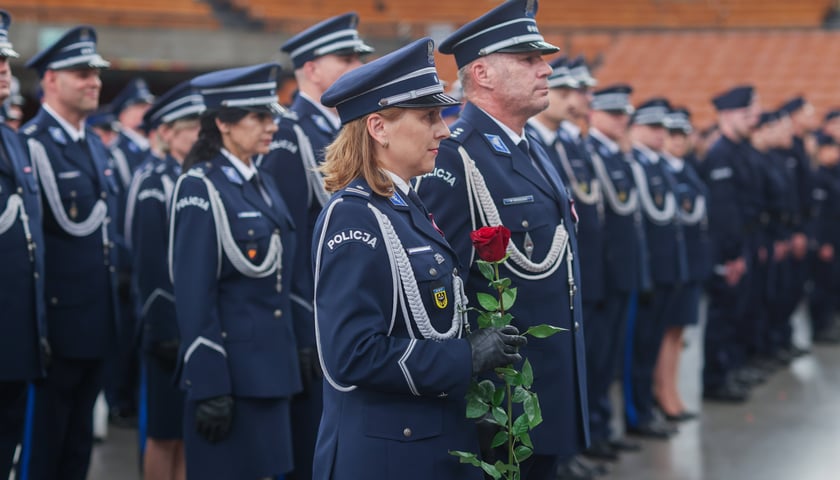 Policjantka w mundurze z różą, w tle policjantki i policjanci podczas uroczystości Święta Policji 2025 w Hali Stulecia