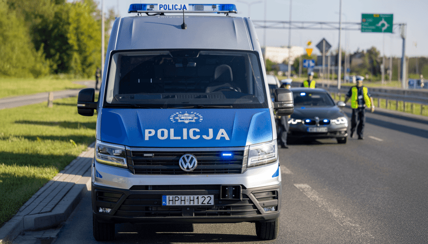 Radiowóz policyjny, w tle policjanci i kontrola drogowa