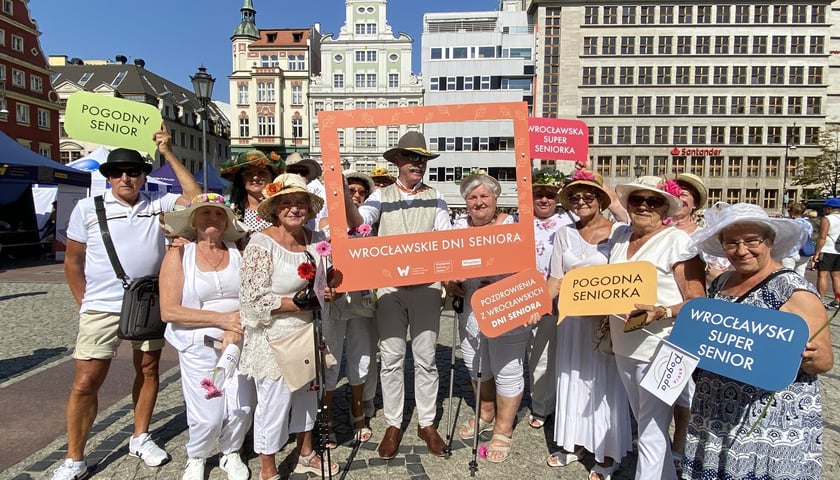 Wrocławscy seniorzy na placu Solnym z Rynku, trzymają pomarańczową ramkę z napisem Wrocławskie Dni Seniora 