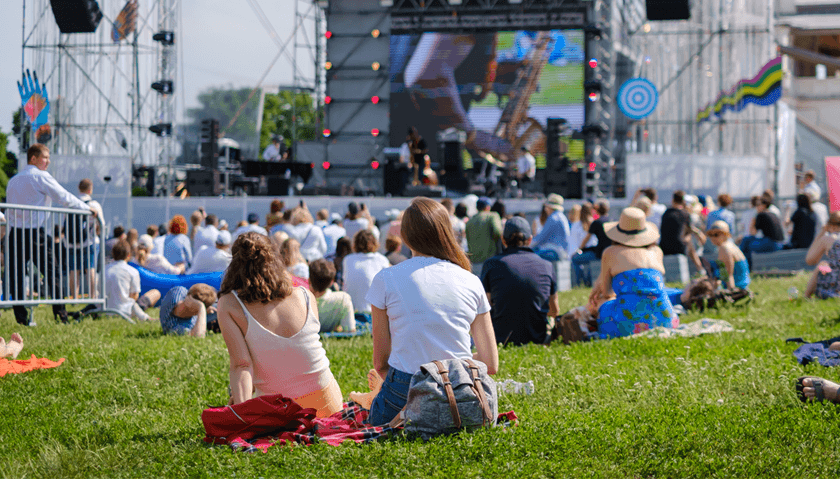 Koncert plenerowy – ludzie siedzą na trawie przed sceną