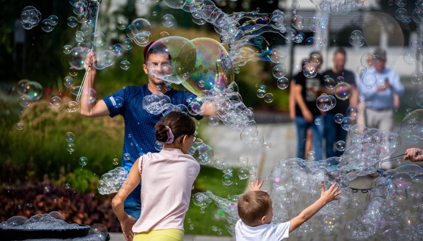 Mężczyzna i dwójka dzieci bawią się bańkami mydlanymi na placu przed hydropolis