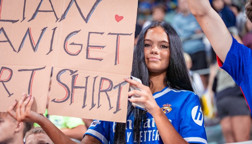 Dziewczyna w niebieskiej koszulce trzyma transparent z hasłem skierowanym do Kyliana Mbappe, 5 września 2025 na Tarczyński Arenie