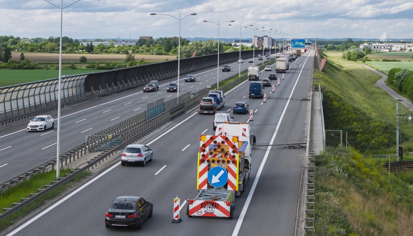 Samochody jadące po AOW i wóz służb drogowych ostrzegający o zamkniętym pasie ruchu. 