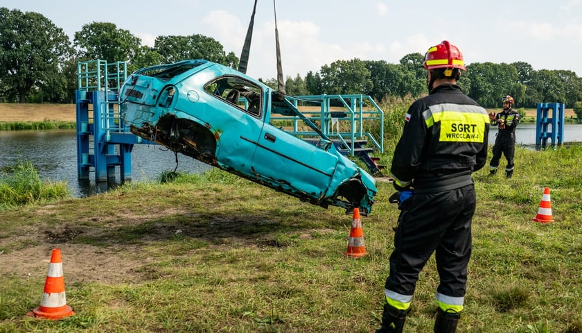 Samochód wyciągnięty z wody, na pierwszym planie strażak