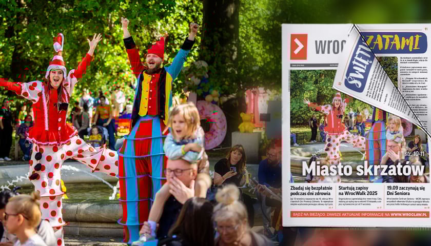 Kobieta i mężczyzna na szczudłach przebrani za krasnale: ona w czerwono-białym stroju i czapce, mężczyzna  w czerwono-niebiesko-żółtym z podniesionymi do góry rękami w parku Staromiejskim podczas Festiwalu Krasnoludków.