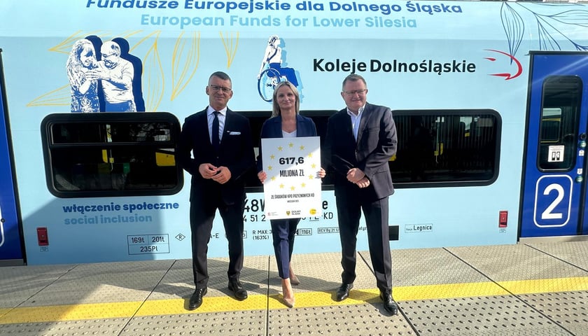 Trzy osoby przed niebieskim pociągiem Kolei Dolnośląskich