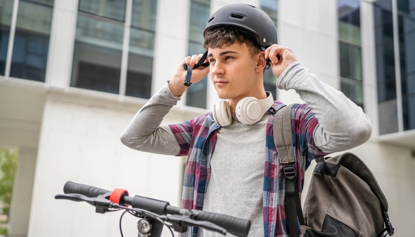 Nastoletni chłopiec na hulajnodze zakładający kask, zdjęcie ilustracyjne