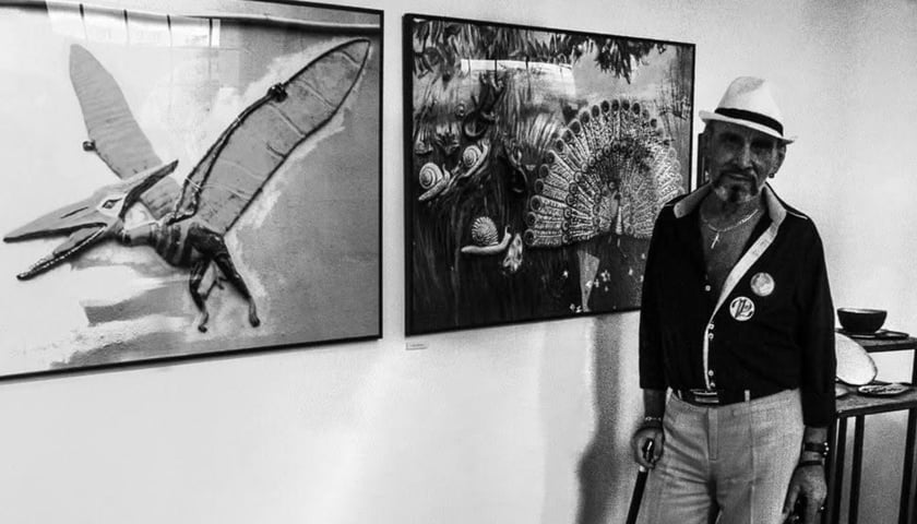 Zenon Dębowski na tle zdjęć swoich płaskorzeźb - pterodaktyla i charakterystycznego pawia
