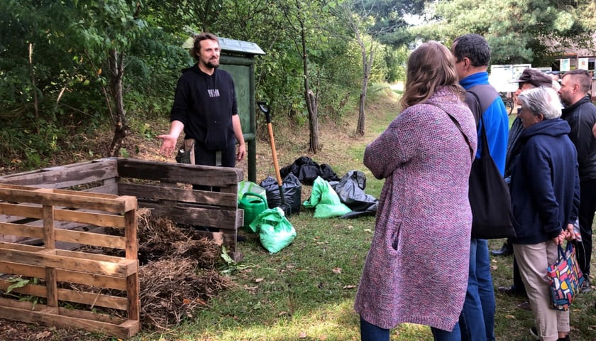 Grupa ludzi przy kompostowniku, w tle drzewa. Warsztaty z kompostowania na ROD „Malina”