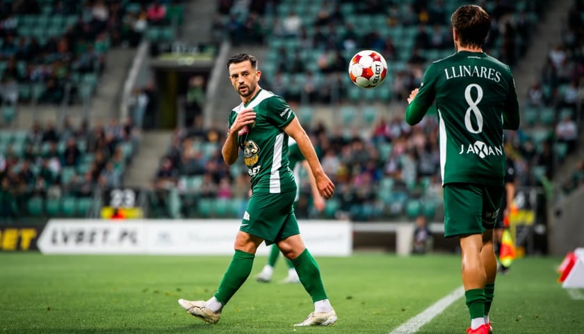 Dwóch piłkarzy w zielonych strojach na boisku podczas meczu. Zawodnicy WKS Śląsk Wrocław wykonują rzut z outu.