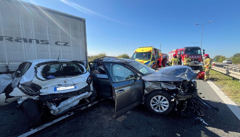 Samochody uszkodzone podczas zderzenia, w tle strażacy. Zderzenie samochodów na S8 na wysokości Oleśnicy