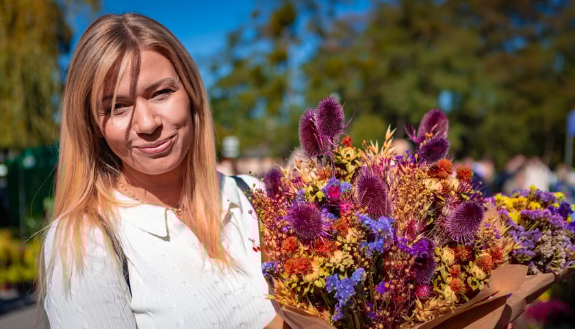 Kiermasz ogrodniczy Pamiętajcie o ogrodach. Na zdjęciu uśmiechnięta, ładna kobieta z bukietem kwiatów