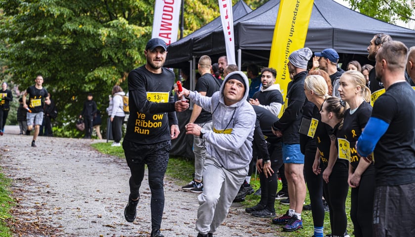 Dwie osoby, które biegnąc przekazują sobie sztafetę