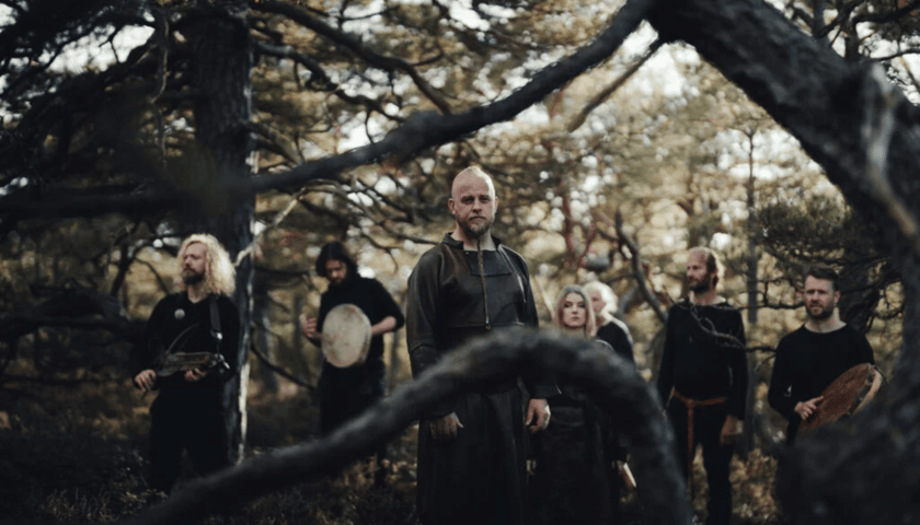 Siedmioro członków norweskiego zespołu folk Wardruna ubranych na czarno w lesie