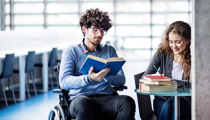 Zdjęcie ilustracyjne - uczeń na wózku inwalidzkim z uczennicą siedzącą przy stoliku 