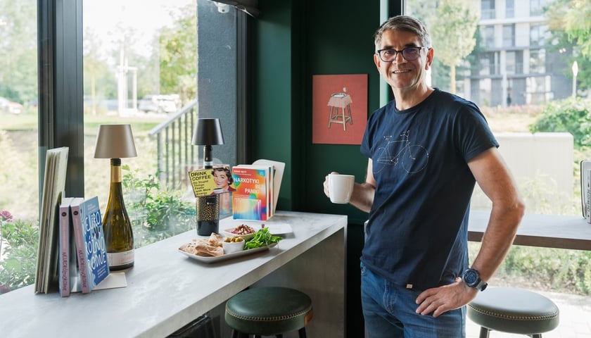 Tomasz Malejki, pomysłodawca i właściciel kawiarnio-winiarni GRONO przy ul. Rusznikarskiej. Na zdjęciu mężczyzna w okularach stoi przy stoliku w ładnym wnętrzu