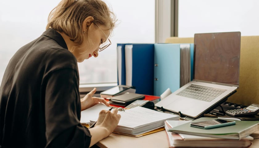 Kobieta przy biurku, pochylona nad dokumentami. Zdjęcie ilustracyjne