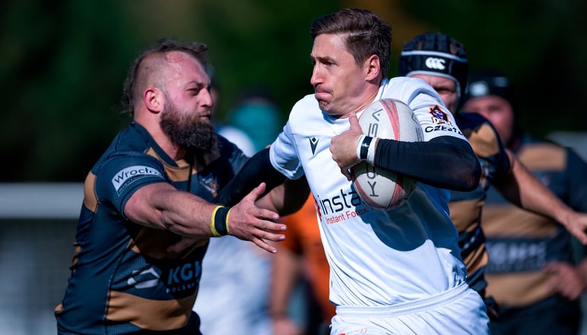 Zawodnik Rugby Wrocław w ciemnej koszulce próbuje zatrzymać biegnącego z piłką przeciwnika.
