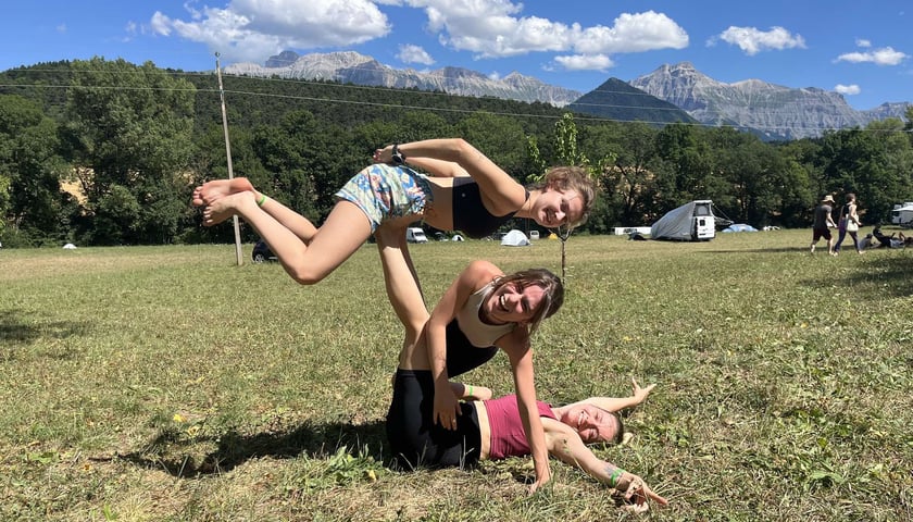 Studentki wykonują figurę akrobatyczną na trawie. Z tyłu widać piękny górski pejzaż.