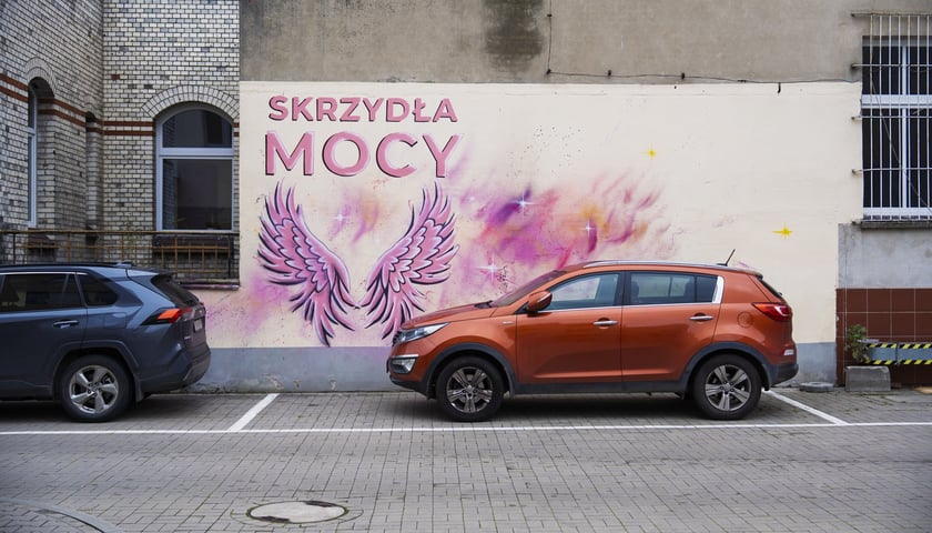 Różowe skrzydła z napisem SKRZYDŁA MOCY namalowane na ścianie szpitala na Hirszfelda