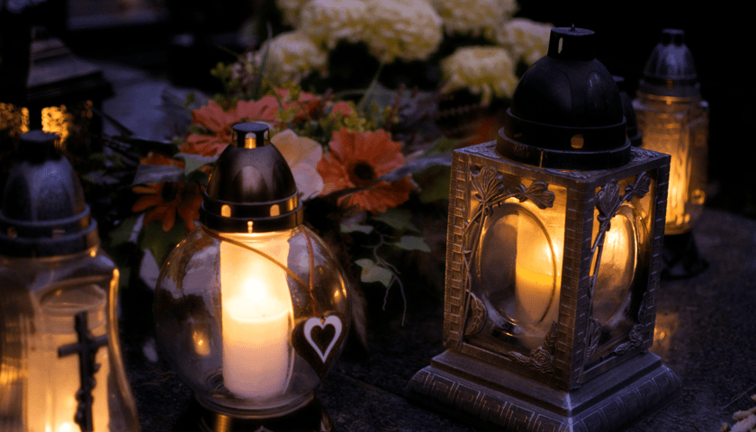 Zdjęcie ilustracyjne: zapalone znicze na grobie, w tle chryzantemy