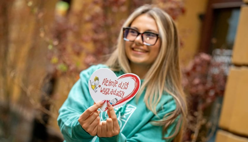 Dziewczyna trzymająca w rękach obrazek z życzliwym hasłem: Pięknie dziś wyglądasz