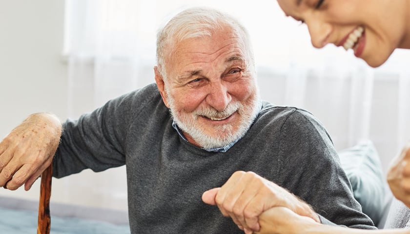 Zdjęcie ilustracyjne: starszy uśmiechnięty mężczyzna trzyma za rękę młodą kobietę